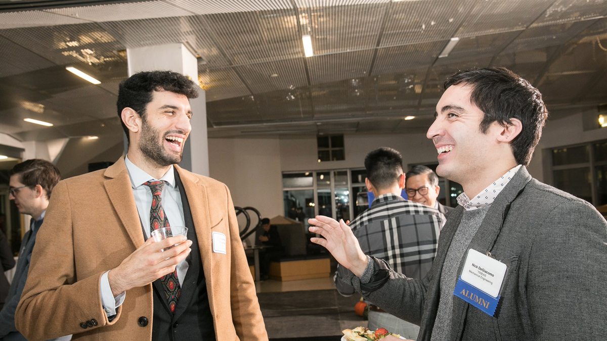 Two men talking and smiling at an indoor reception