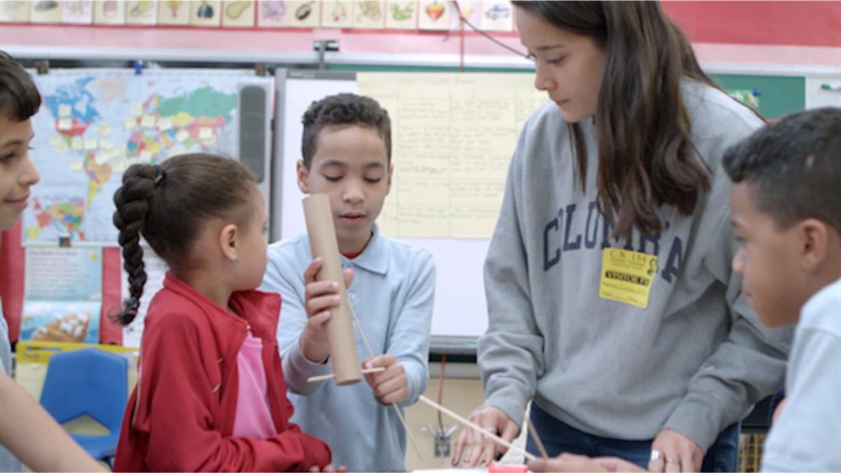 An adult in a Columbia sweatshirt helps children with a hands-on classroom activity